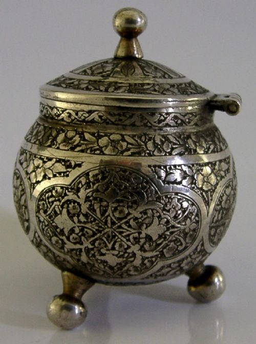 An antique hand-engraved solid silver mustard pot featuring arabesque foliage patterns, a hinged lid with finial, a spoon aperture, and three ball feet. View III