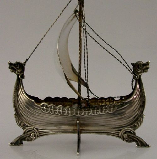A detailed solid silver model of a Viking longship featuring a dragon head prow, raised sail, pennant flag, and miniature shields along the gunwale. View IX