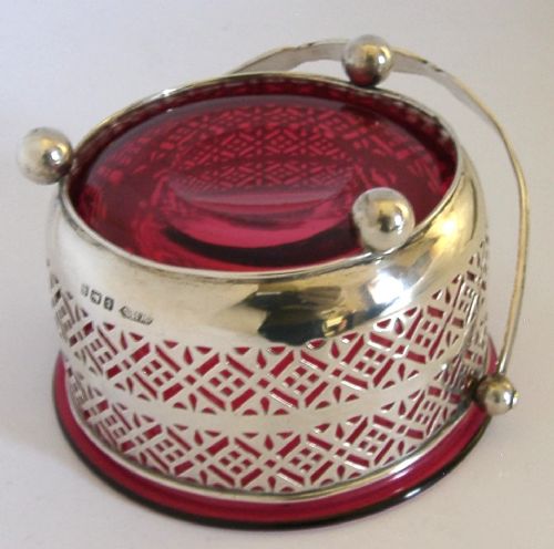 An Edwardian sterling silver pierced basket featuring a lattice geometric pattern, a swing handle, and a fitted cranberry red glass liner. View VII