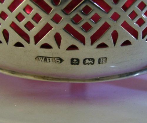 An Edwardian sterling silver pierced basket featuring a lattice geometric pattern, a swing handle, and a fitted cranberry red glass liner. View IX