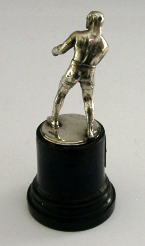 A silver-plated figurine of a boxer in a fighting stance mounted on a dark cylindrical wooden base with an engraved inscription plate. View II