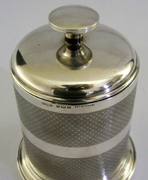 A cylindrical Art Deco sterling silver cigarette dispenser featuring engine-turned patterning, a central polished silver band, and a round knob finial on top. View II