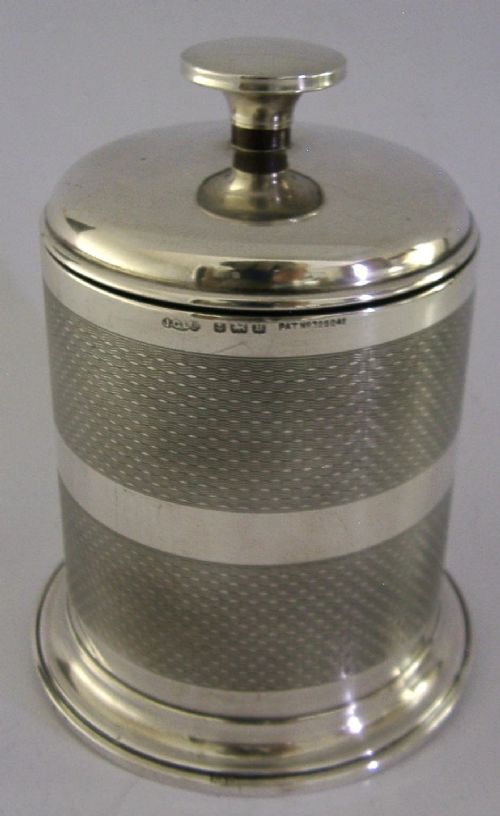 A cylindrical Art Deco sterling silver cigarette dispenser featuring engine-turned patterning, a central polished silver band, and a round knob finial on top. View III