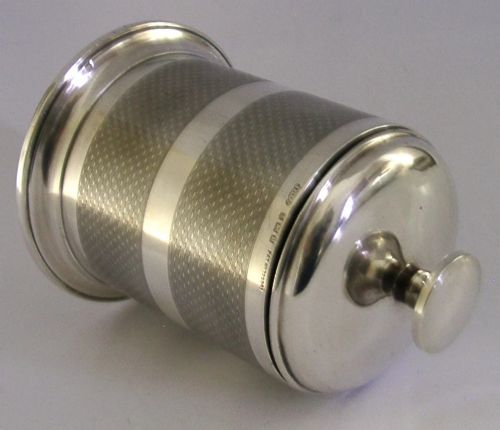 A cylindrical Art Deco sterling silver cigarette dispenser featuring engine-turned patterning, a central polished silver band, and a round knob finial on top. View V