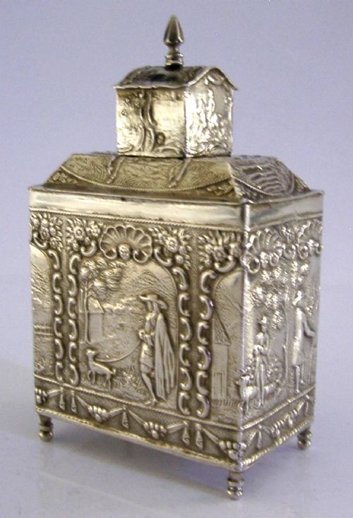 A rectangular solid silver tea caddy featuring relief-embossed pastoral scenes, turned feet, and a finial lid. View III