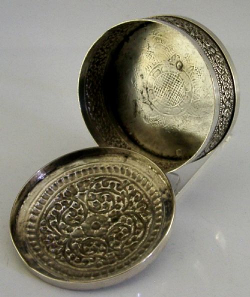 A circular antique silver trinket box with a lidded top featuring dense relief floral scrollwork and an oxidised background. View IV