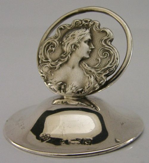 An Art Nouveau sterling silver menu holder featuring a relief profile of a maiden with flowing hair framed by a circular wire loop. View II