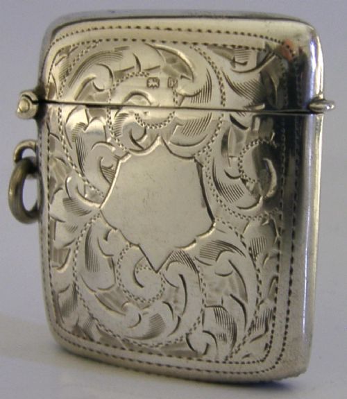 An antique sterling silver vesta case featuring hand-engraved foliate scrollwork, a central shield cartouche, a hinged lid, and a side suspension ring. View II