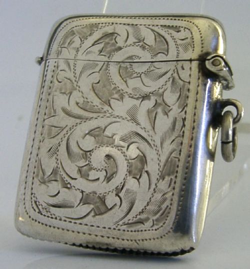 An antique sterling silver vesta case featuring hand-engraved foliate scrollwork, a central shield cartouche, a hinged lid, and a side suspension ring. View III