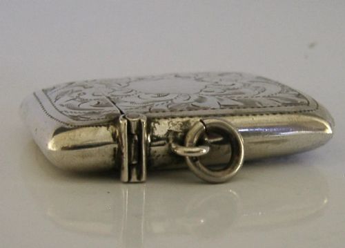 An antique sterling silver vesta case featuring hand-engraved foliate scrollwork, a central shield cartouche, a hinged lid, and a side suspension ring. View V
