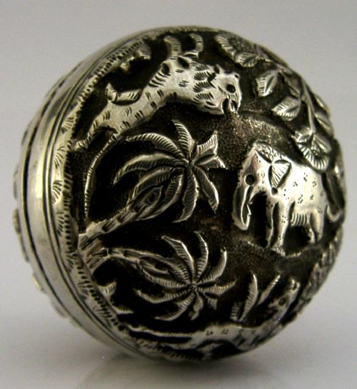 A circular solid silver box with relief repousse carvings depicting an elephant and palm trees in a jungle landscape. View II