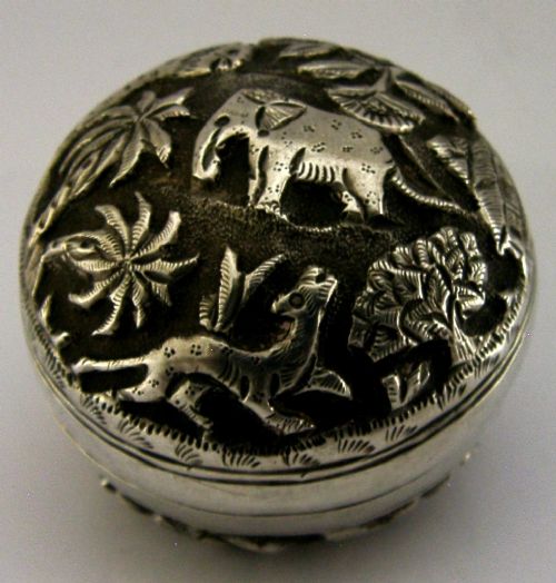 A circular solid silver box with relief repousse carvings depicting an elephant and palm trees in a jungle landscape. View IV