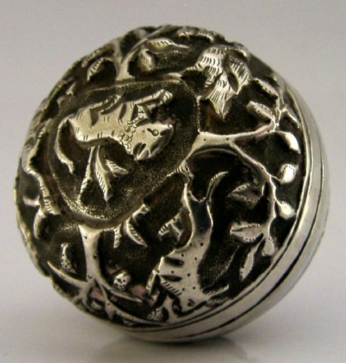 A circular solid silver box with relief repousse carvings depicting an elephant and palm trees in a jungle landscape. View V