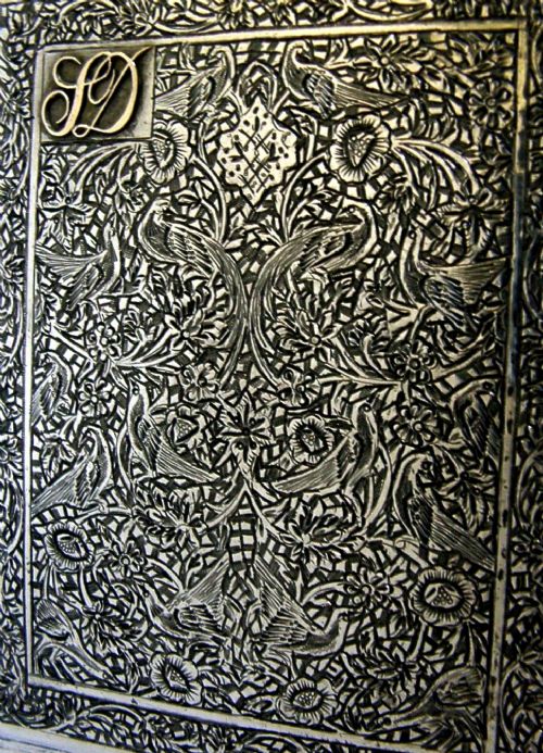 A rectangular solid silver cigarette case featuring dense hand-engraved bird and foliate patterns with a gold monogram in the upper corner. View II
