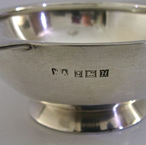 A polished solid sterling silver shallow whisky quaich cup with two flat side lugs resting on a circular raised foot. View II