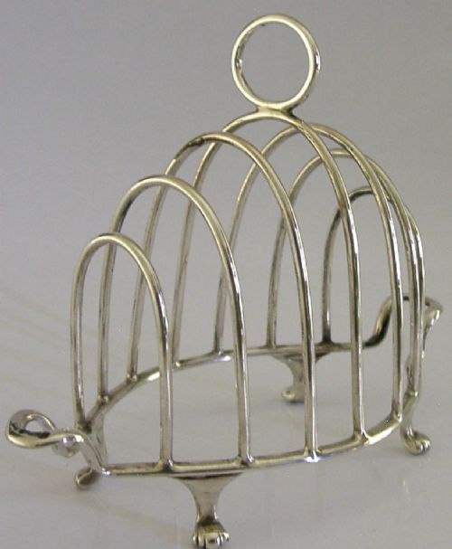 A 1925 English sterling silver six-slice toast rack featuring arched wire dividers, a top ring handle, and small paw feet. View IV