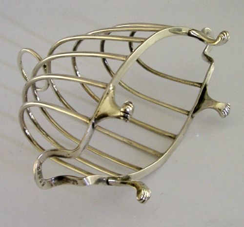 A 1925 English sterling silver six-slice toast rack featuring arched wire dividers, a top ring handle, and small paw feet. View V
