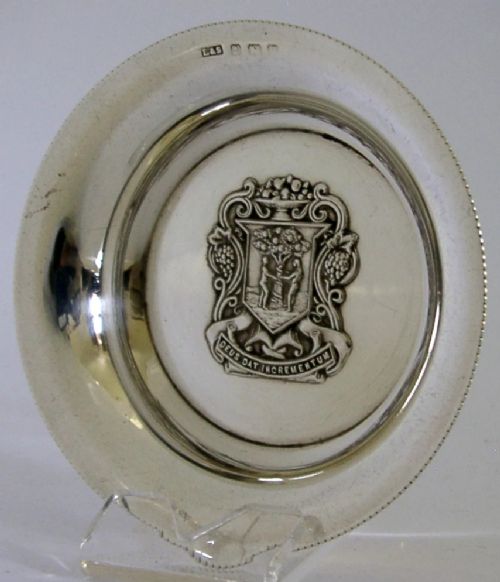 A circular sterling silver dish featuring the embossed coat of arms of the Worshipful Company of Fruiterers in the centre with hallmarks near the rim.