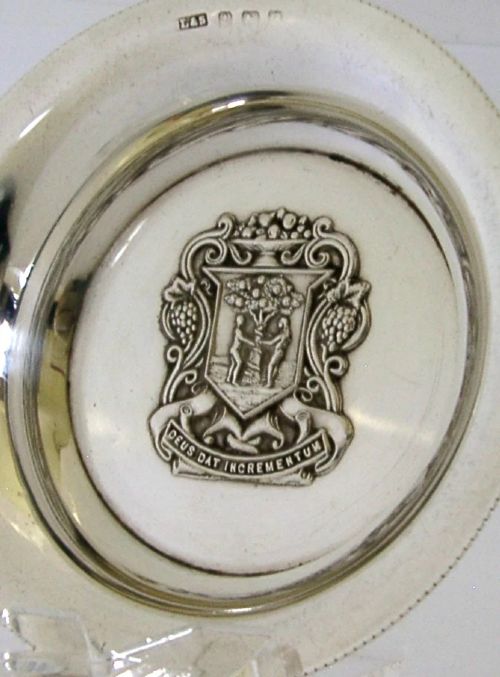 A circular sterling silver dish featuring the embossed coat of arms of the Worshipful Company of Fruiterers in the centre with hallmarks near the rim. View IV