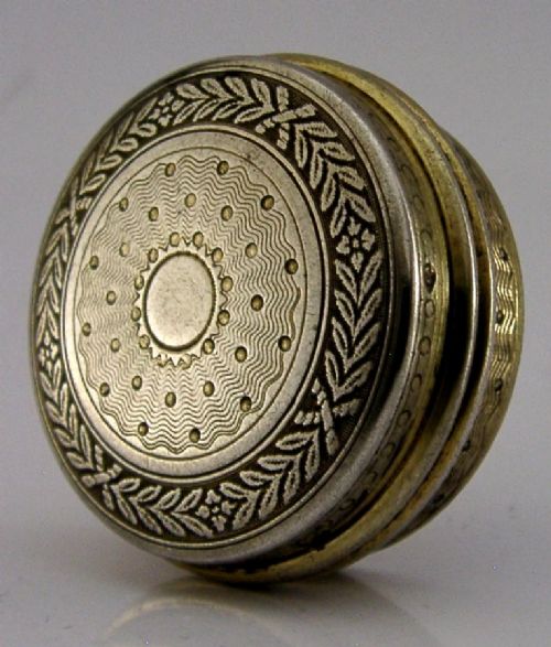 A circular French sterling silver gilt trinket box featuring engine-turned guilloche detailing and a decorative laurel leaf border.