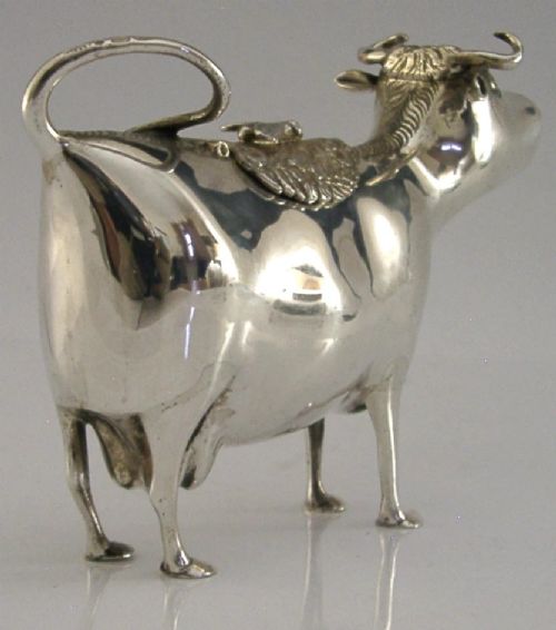 A sterling silver novelty cow creamer featuring a hollow cast body, a hinged lid decorated with floral motifs on the back, and a looped tail handle. View VII