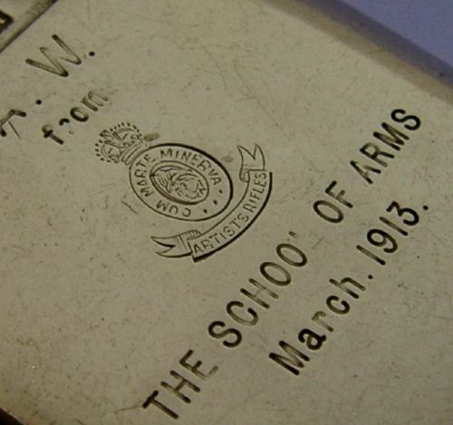 An Edwardian sterling silver vesta case featuring engraved military crests, text reading THE SCHOOL OF ARMS March. 1913, a side attachment ring, and a hinged lid. View II