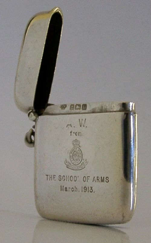 An Edwardian sterling silver vesta case featuring engraved military crests, text reading THE SCHOOL OF ARMS March. 1913, a side attachment ring, and a hinged lid. View IV