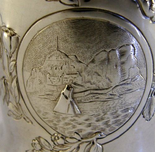 A Victorian sterling silver tankard mug featuring detailed relief floral decoration, a landscape roundel, a scroll handle, and a gilt interior. View II