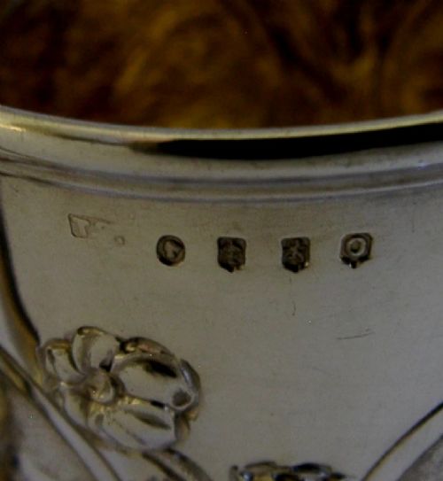 A Victorian sterling silver tankard mug featuring detailed relief floral decoration, a landscape roundel, a scroll handle, and a gilt interior. View XII