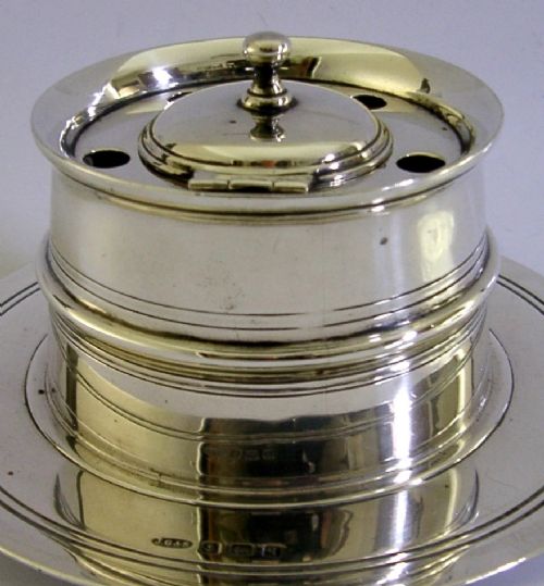 A solid sterling silver circular capstan inkwell featuring a hinged central lid and pierced quill holes set upon a wide dished base with visible hallmarks. View II