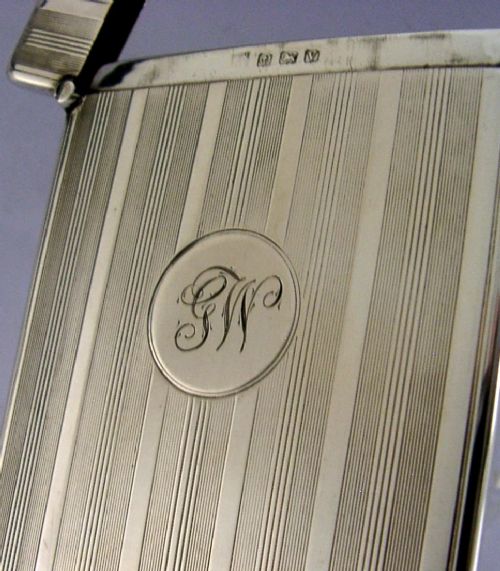 An open rectangular sterling silver card case with linear engine-turned patterns and a central circular monogrammed cartouche. View IV