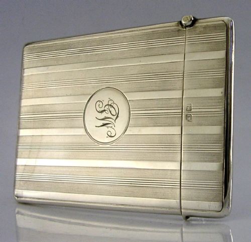 An open rectangular sterling silver card case with linear engine-turned patterns and a central circular monogrammed cartouche. View VII