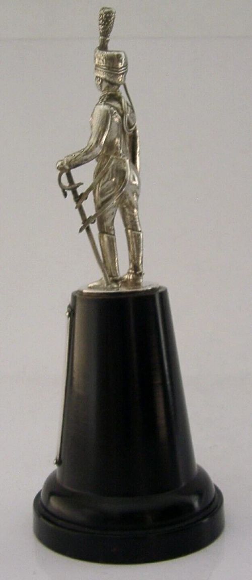 A sterling silver figurine depicting a Royal Hussar soldier in full military dress uniform, standing atop a tapered black wooden plinth with a silver presentation plaque. View V