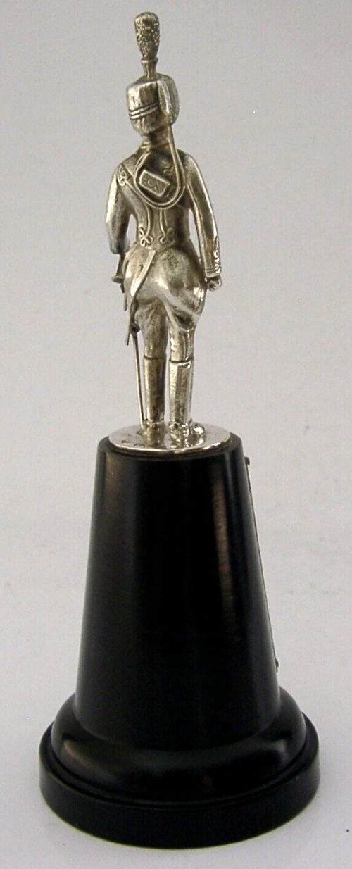 A sterling silver figurine depicting a Royal Hussar soldier in full military dress uniform, standing atop a tapered black wooden plinth with a silver presentation plaque. View VIII