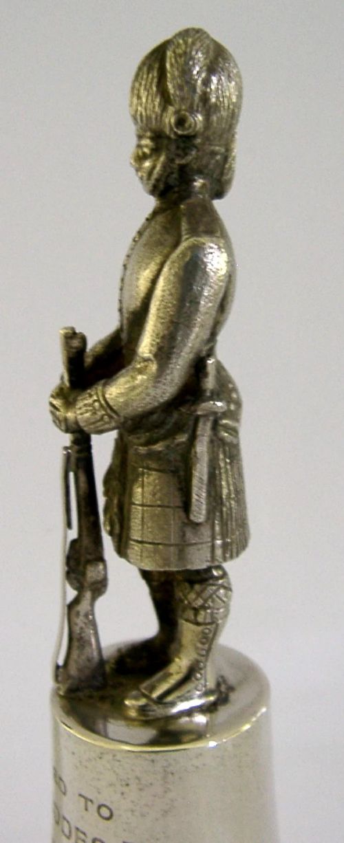 A polished sterling silver table bell topped with a sculpted Black Watch soldier figurine and featuring engraved regimental lettering on the bell body. View VI