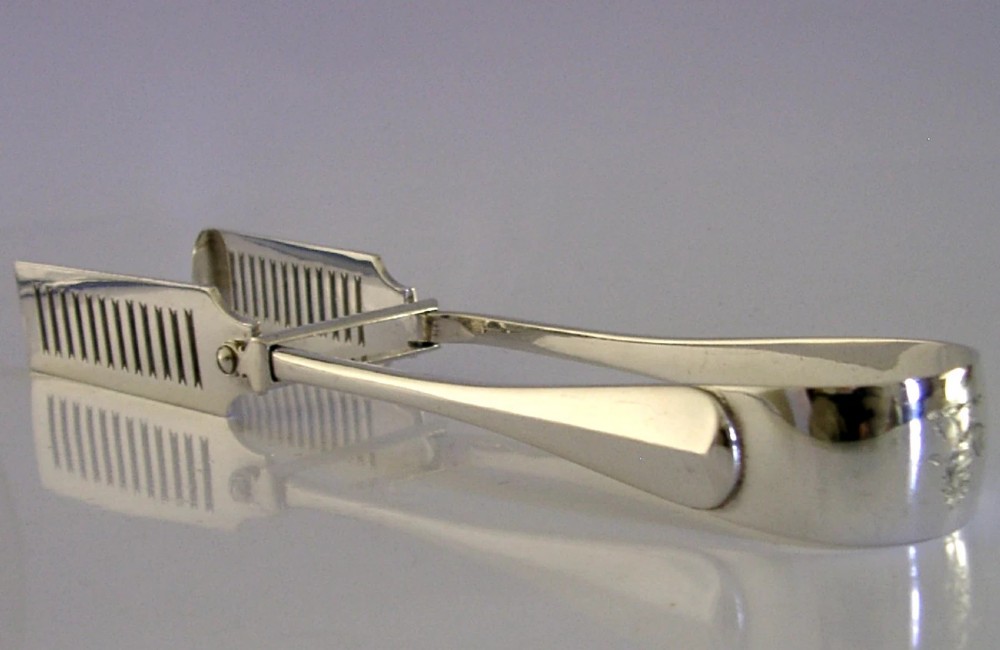 Edwardian sterling silver serving tongs featuring slotted rectangular blades and an engraved crest on the curved handle.