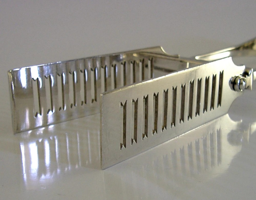 Edwardian sterling silver serving tongs featuring slotted rectangular blades and an engraved crest on the curved handle. View II