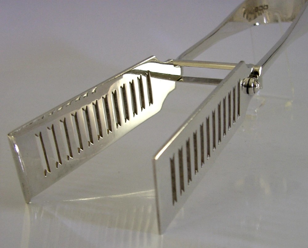 Edwardian sterling silver serving tongs featuring slotted rectangular blades and an engraved crest on the curved handle. View IV