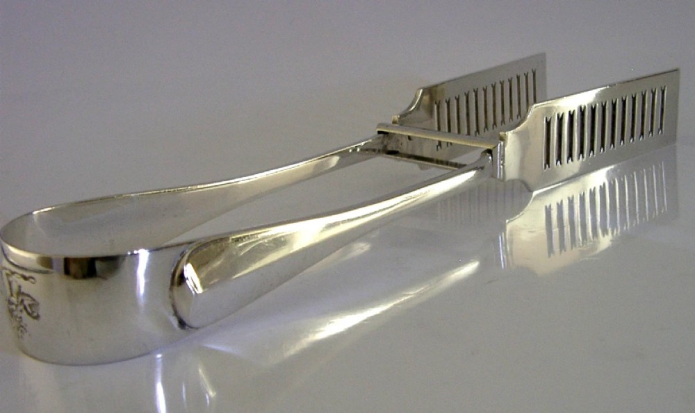 Edwardian sterling silver serving tongs featuring slotted rectangular blades and an engraved crest on the curved handle. View V