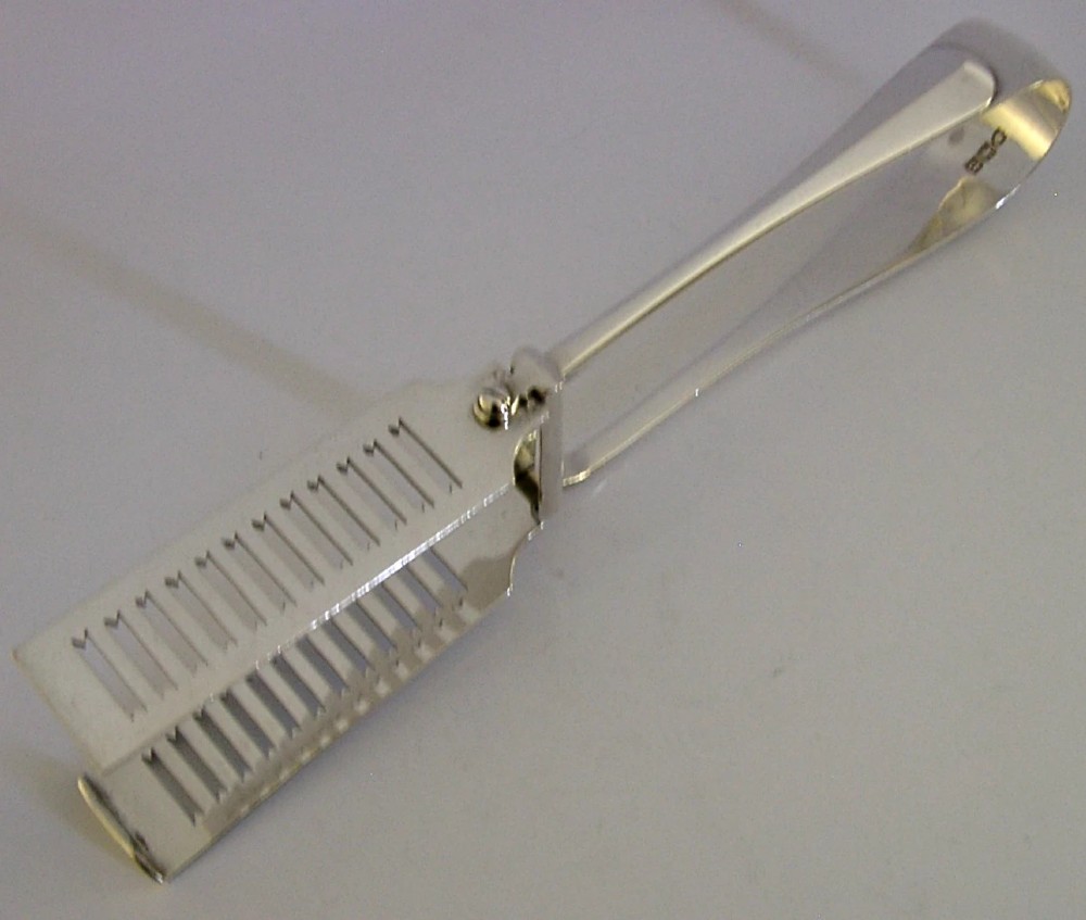 Edwardian sterling silver serving tongs featuring slotted rectangular blades and an engraved crest on the curved handle. View VII