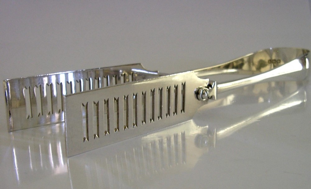 Edwardian sterling silver serving tongs featuring slotted rectangular blades and an engraved crest on the curved handle. View VIII