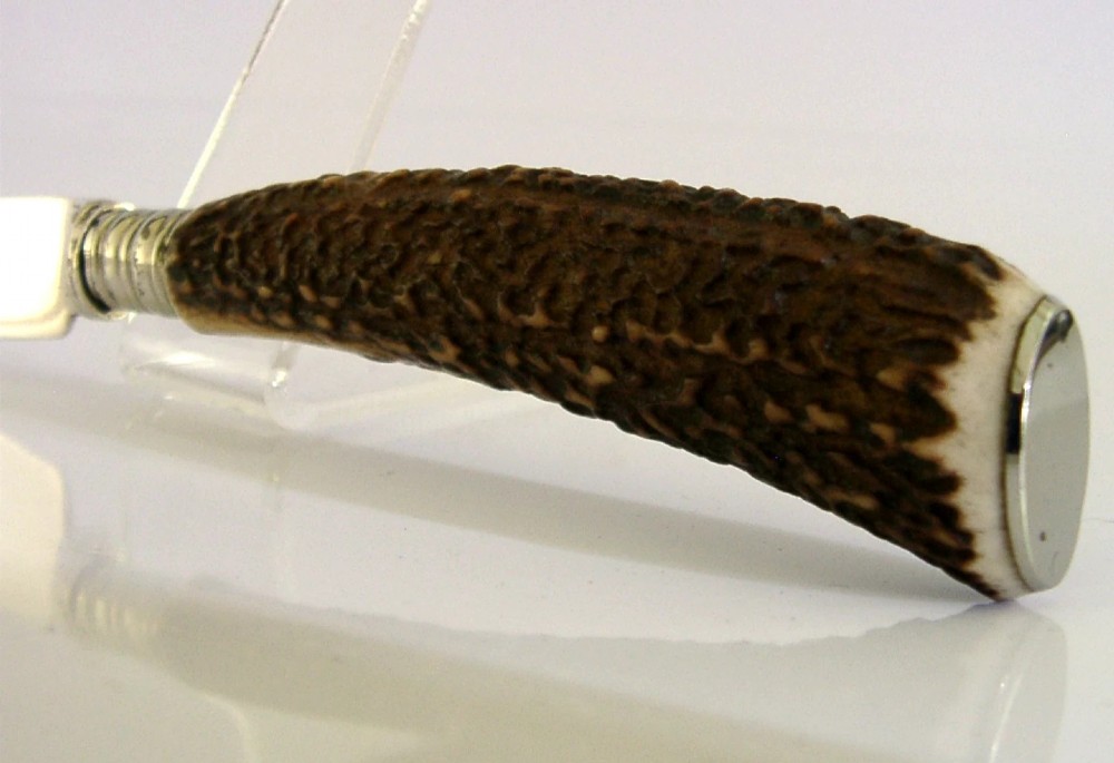 An Edwardian sterling silver cheese knife featuring a curved silver blade with hallmarks and a dark brown textured stag antler handle. View III