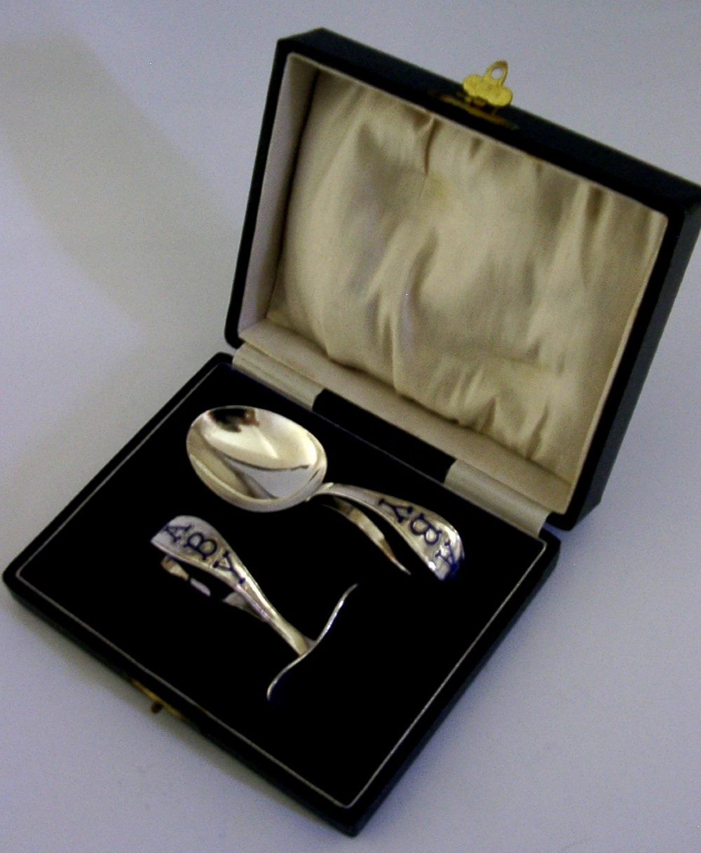 A sterling silver spoon and pusher set featuring blue enamel lettering inside an open black presentation box with white silk lining.
