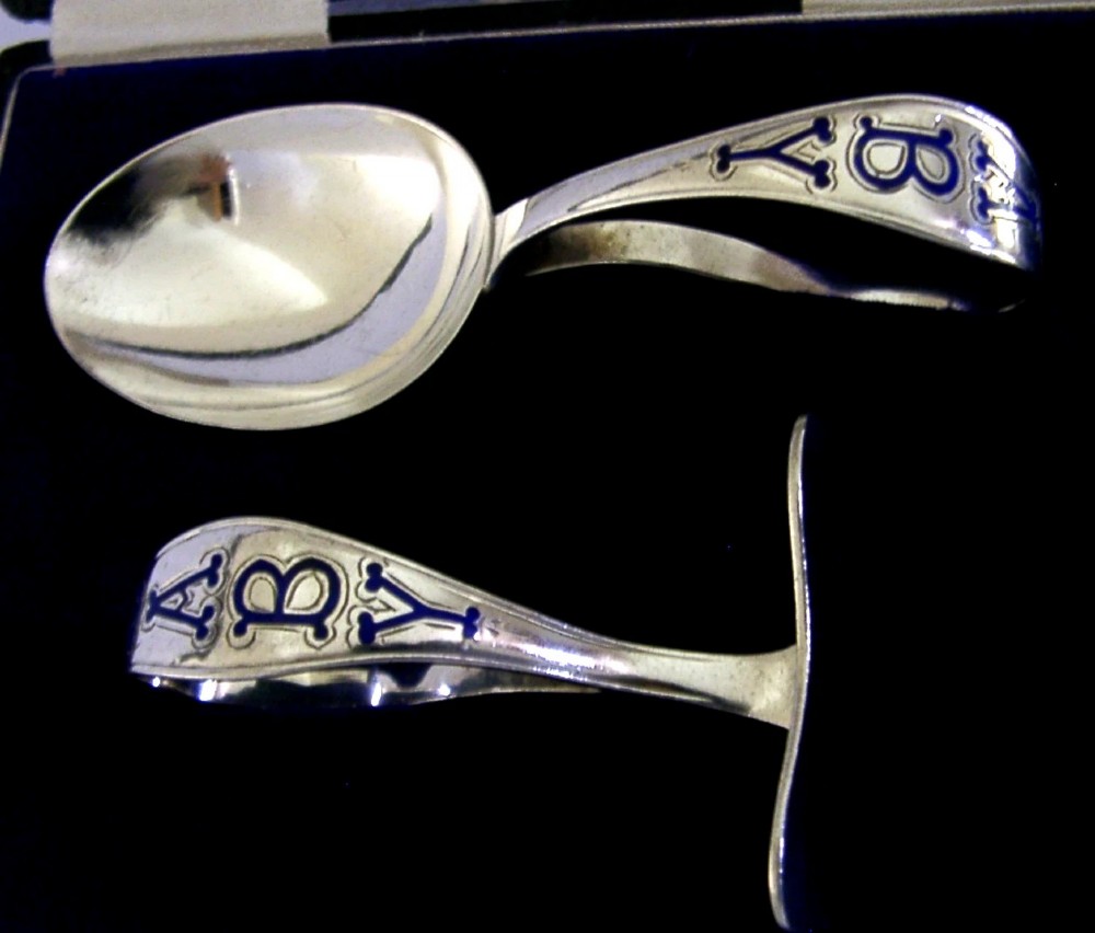 A sterling silver spoon and pusher set featuring blue enamel lettering inside an open black presentation box with white silk lining. View II
