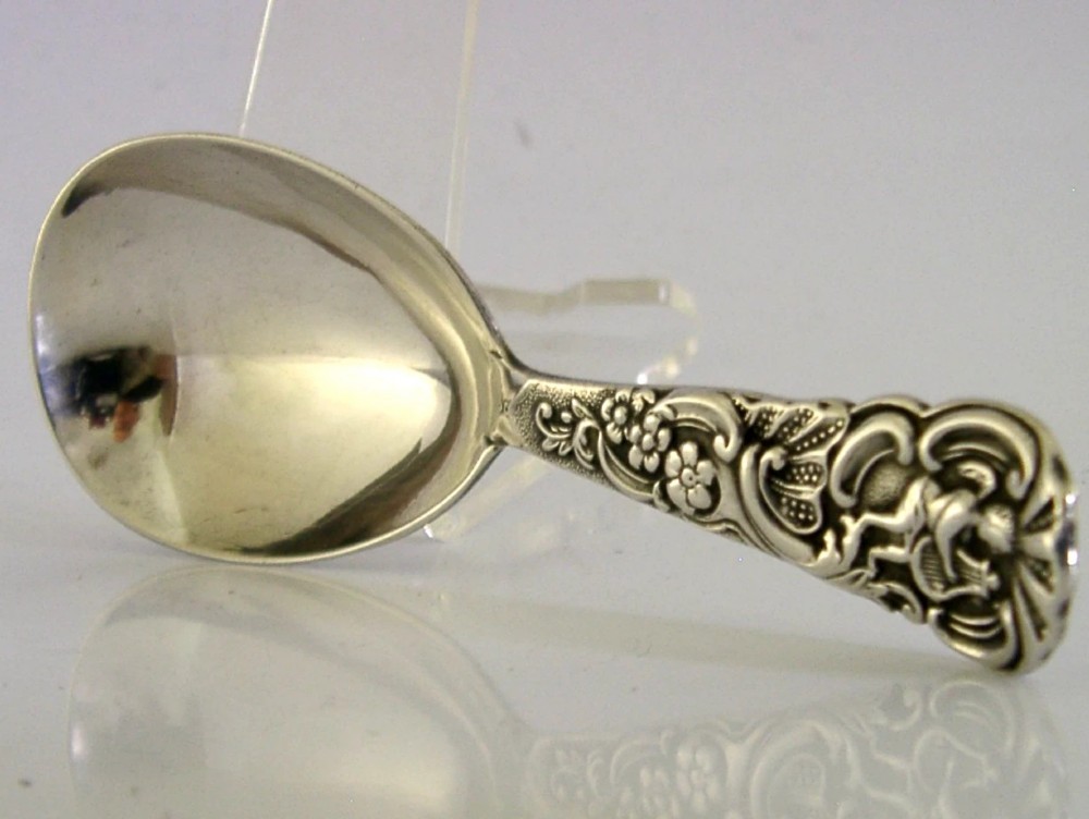 An Edwardian sterling silver tea caddy spoon with a smooth ovate bowl and an embossed handle depicting an angel holding a harp.