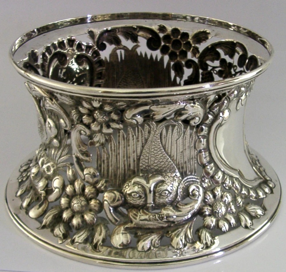 An hourglass-shaped sterling silver dish ring featuring intricately pierced fretwork with floral motifs, scrolls, and marine life details.
