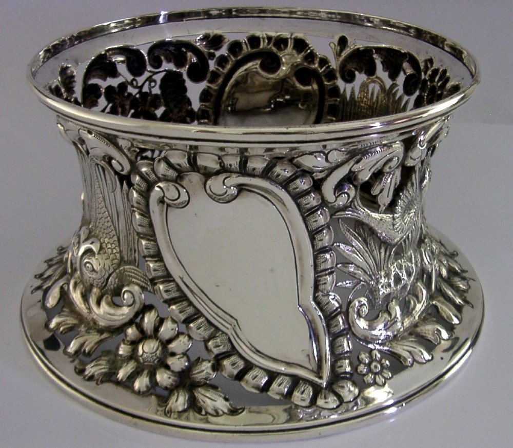 An hourglass-shaped sterling silver dish ring featuring intricately pierced fretwork with floral motifs, scrolls, and marine life details. View VI