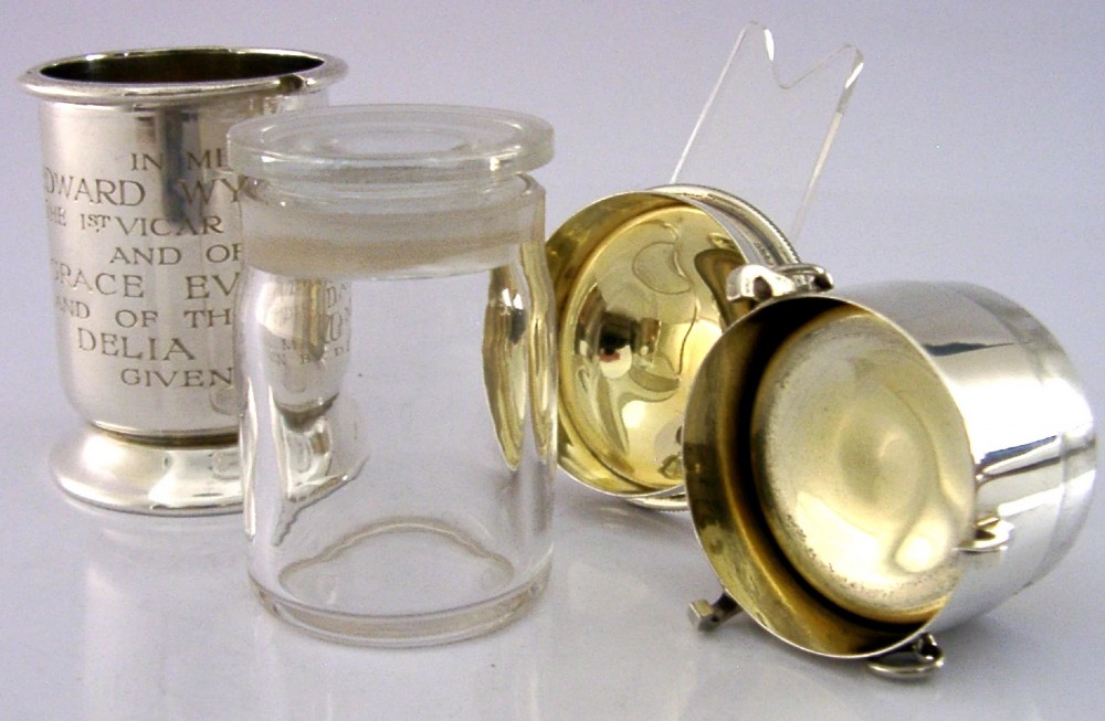 A cylindrical sterling silver pyx vessel with an engraved commemorative inscription, side suspension rings, and a fitted lid on a pedestal base. View II