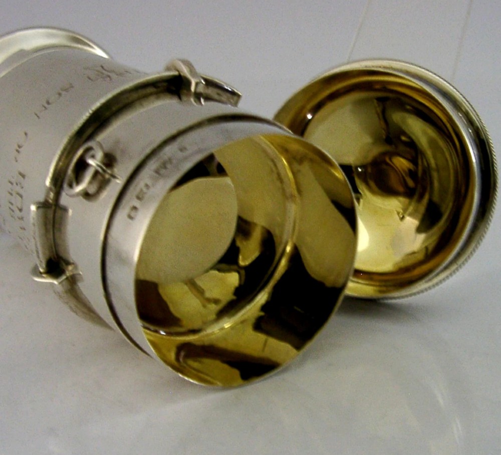 A cylindrical sterling silver pyx vessel with an engraved commemorative inscription, side suspension rings, and a fitted lid on a pedestal base. View IV