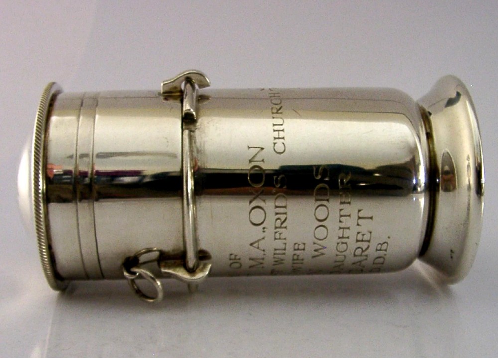 A cylindrical sterling silver pyx vessel with an engraved commemorative inscription, side suspension rings, and a fitted lid on a pedestal base. View IX
